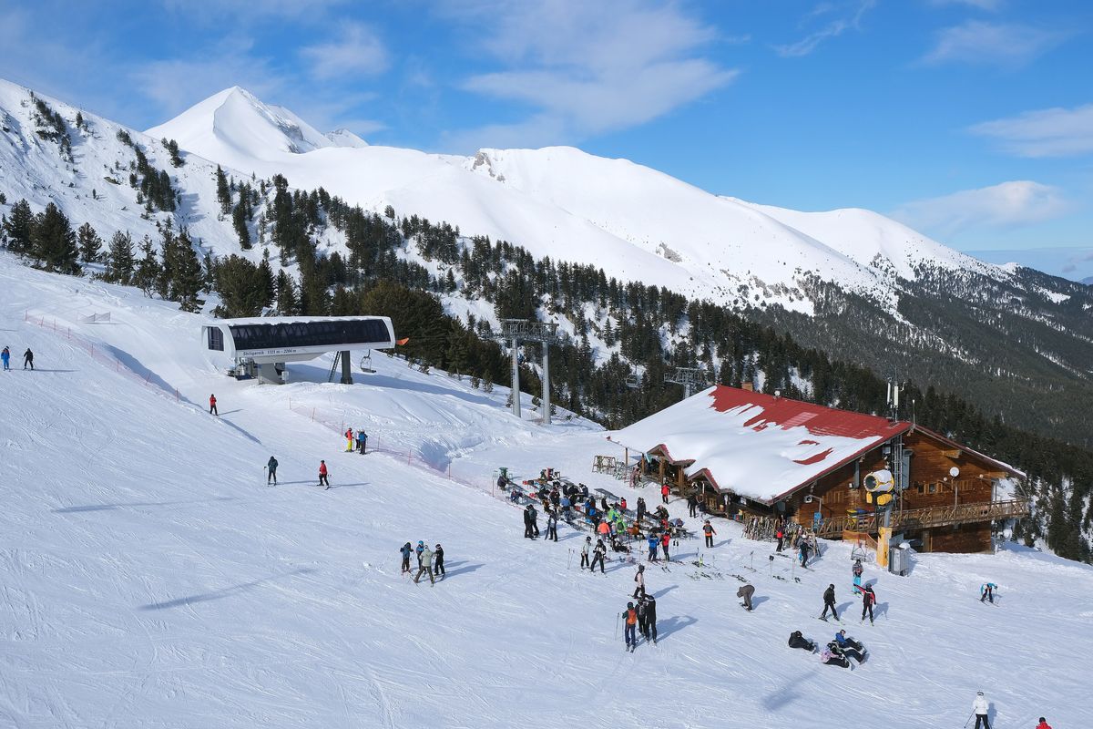 Skipiste in Bansko mit Skifahrern und verschneitem Pirin-Gebirge