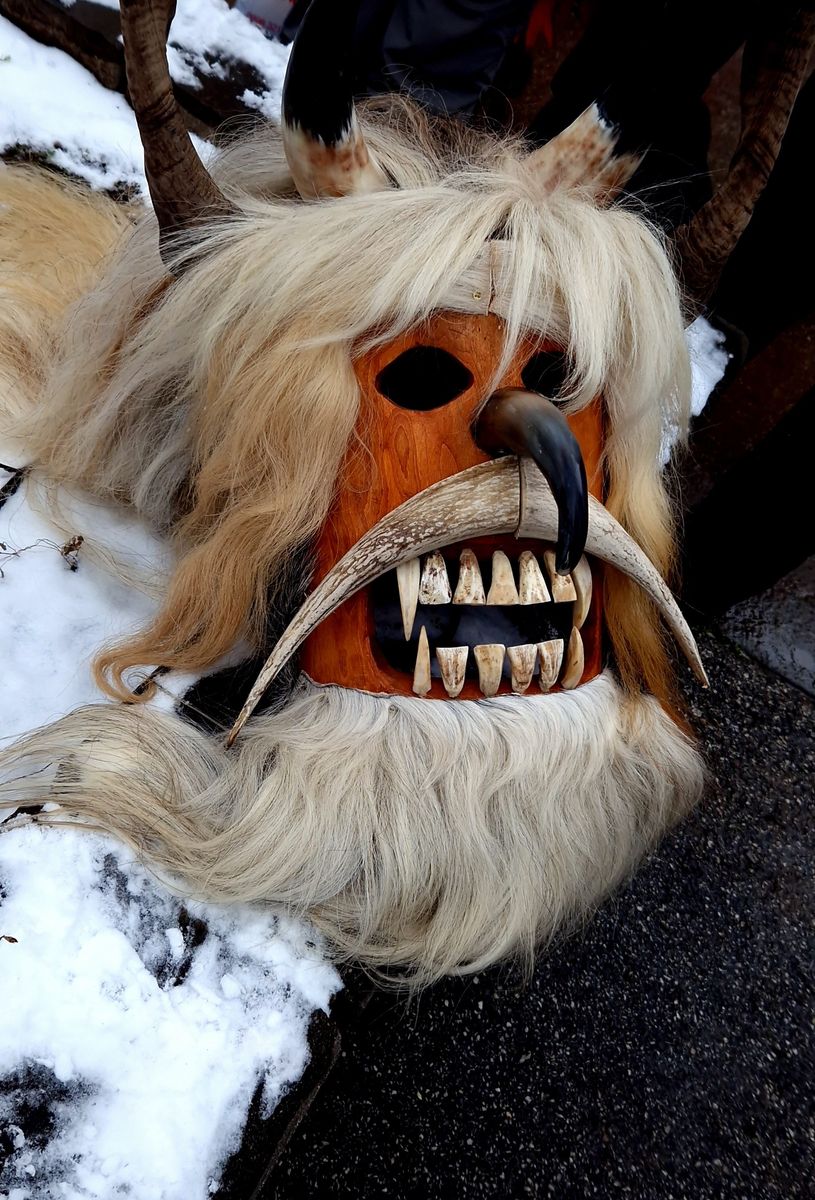 Nahaufnahme einer Kukeri-Maske mit Hörnern, Federn und bunten Verzierungen